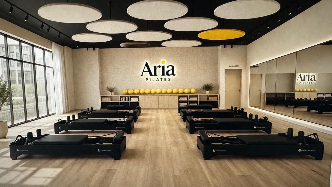 Rendering of Aria Pilates studio interior — open space with reformers, backlit Aria wordmark on the main wall, and natural light from floor-to-ceiling windows
